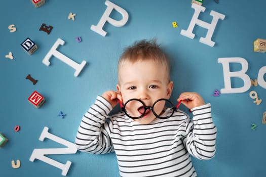 One year old child lying with spectacles and letters on blue background