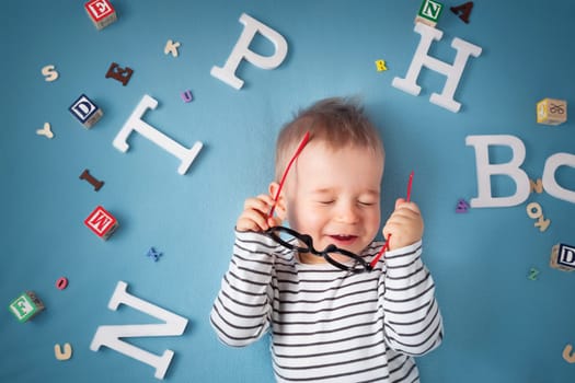 One year old child lying with spectacles and letters on blue background