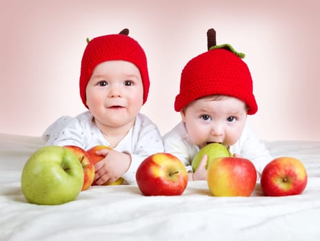 two cute six month old babies lying in hats on soft blanket with apples