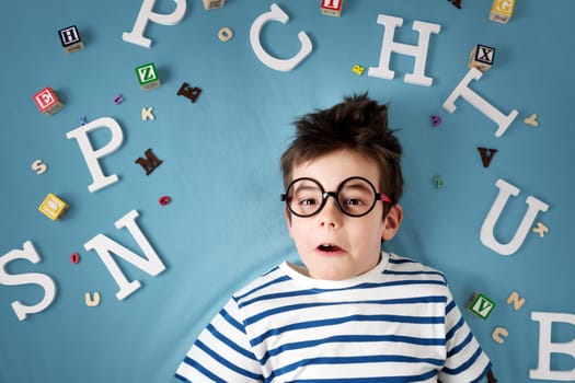 seven years old child lying with glasses and letters on blue background
