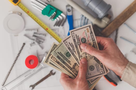 In the foreground men's hands count the costs of repairs or construction. View from above. Building supplies and a drawing in the background.