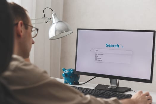 Unemployed man looking for work on the Internet sitting at a computer at home.