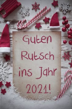 Vertical Paper With German Text Guten Rutsch 2021 Means Happy New Year. White Wooden Background With Snow. Retro Flat Lay With Christmas Decoration, Like Candy Sticks, Sled, Santa Hat And Snowflakes