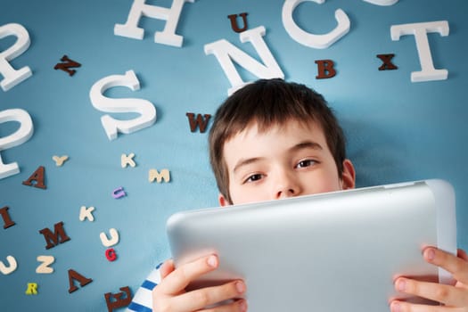 seven years old child lying with tablet and letters on blue background