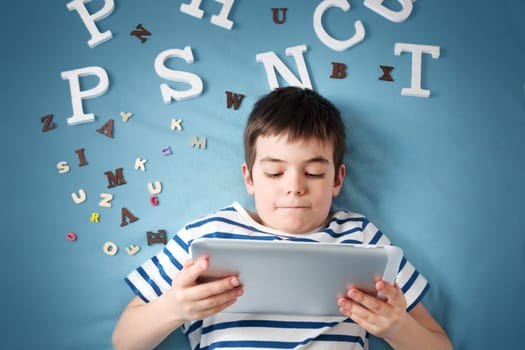 seven years old child lying with tablet and letters on blue background