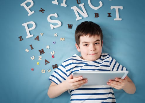 seven years old child lying with tablet and letters on blue background