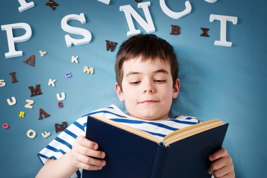 seven years old child lying with book and letters on blue background