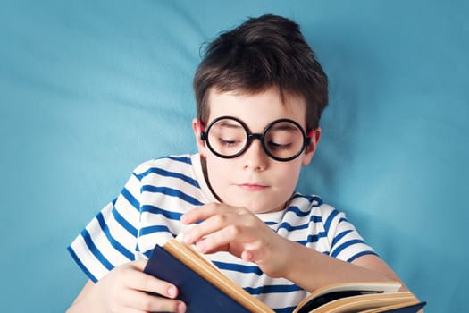 seven years old child lying with book on blue background