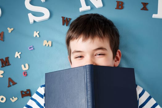 seven years old child lying with book and letters on blue background