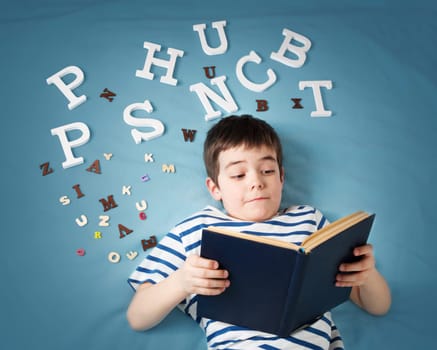 seven years old child lying with book and letters on blue background