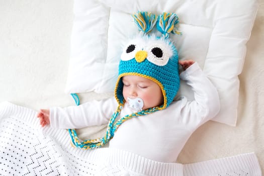 seven month old boy sleeping in the bed in owl hat