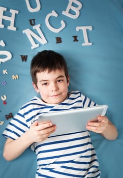seven years old child lying with tablet and letters on blue background