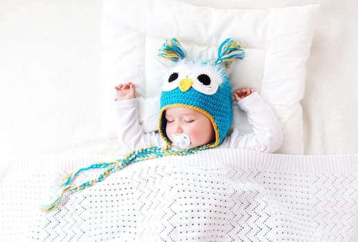 seven month old boy sleeping in the bed in owl hat