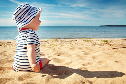 Nine month old baby boy sitting on the beach in beautiful summer day