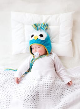 seven month old boy sleeping in the bed in owl hat
