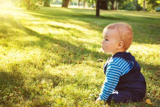 little nine month old baby sitting in the park in beautiful evening