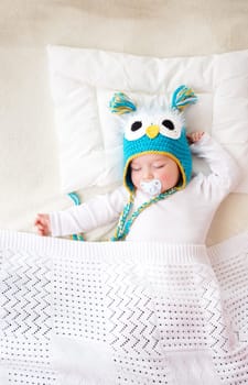 seven month old boy sleeping in the bed in owl hat