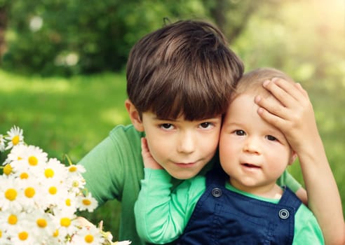 Two lovely brothers sitting in park with flowers hugging