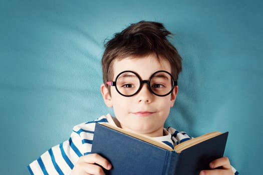 seven years old child lying with book on blue background
