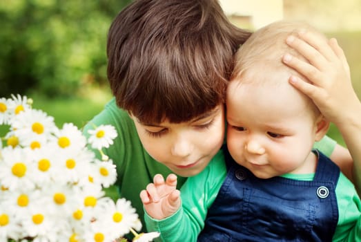Two lovely brothers sitting in park with flowers hugging