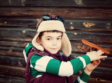 Boy playing in aviator hat with old plane at countryside