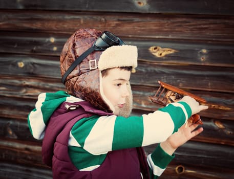 Boy playing in aviator hat with old plane at countryside