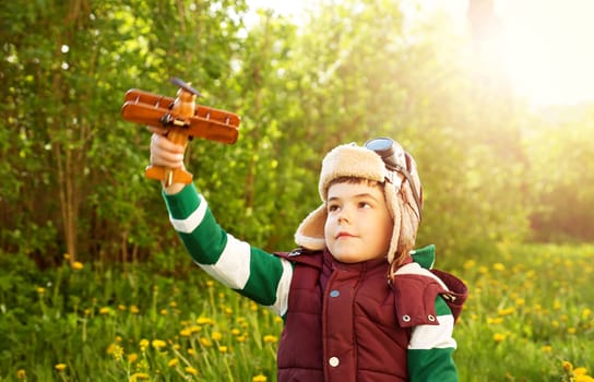 Boy playing in aviator hat with old plane at countryside