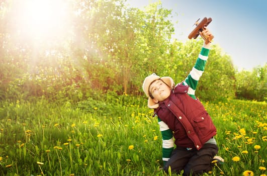 Boy playing in aviator hat with old plane at countryside