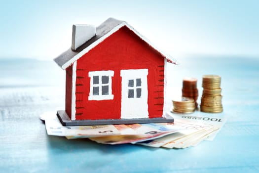 Red house model on wooden background with banknotes and coins