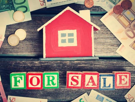 Red house model on wooden background with banknotes and coins