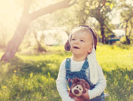 Boy playing in aviator hat with teddy bear in the garden