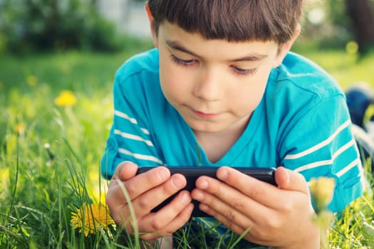 Child lying on the grass in summer suth mobile phone in summer