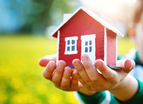 childs hands holding red wooden model house