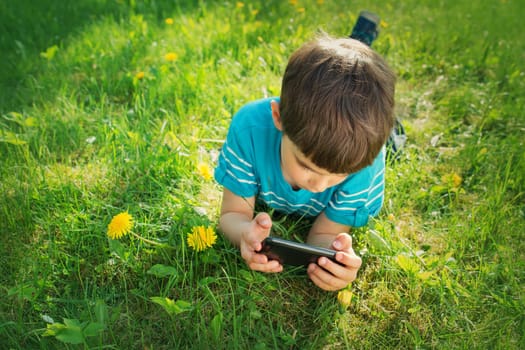 Child lying on the grass in summer suth mobile phone in summer