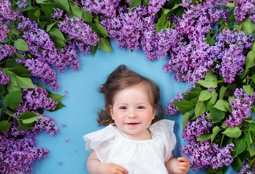 pretty little baby girl lying on blue background with lilac flowers