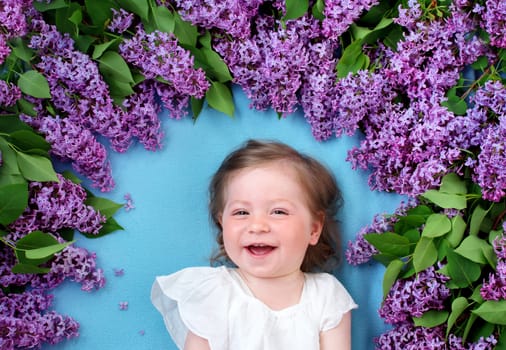 pretty little baby girl lying on blue background with lilac flowers