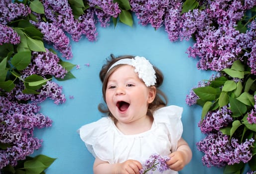 pretty little baby girl lying on blue background with lilac flowers