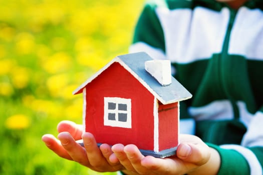childs hands holding red wooden model house