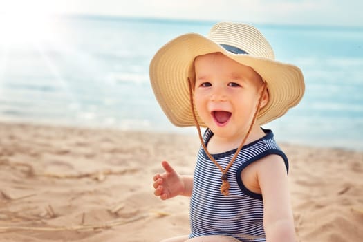 one year old boy sitting at the beach in straw hat