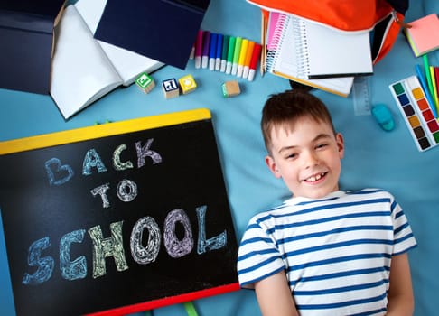 child lying on blue blanket with blackboard and various school accessories