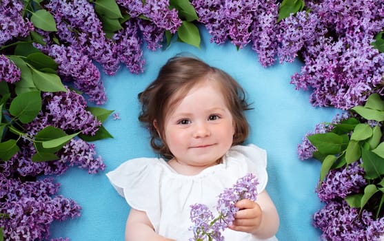 pretty little baby girl lying on blue background with lilac flowers
