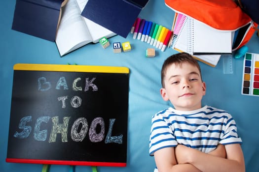 child lying on blue blanket with blackboard and various school accessories