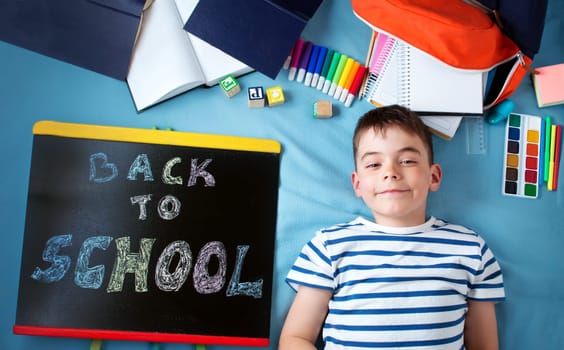 child lying on blue blanket with blackboard and various school accessories