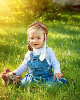 Boy playing in aviator hat with teddy bear in the garden