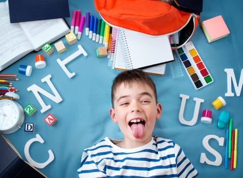 child lying on blue blanket with various school accessories