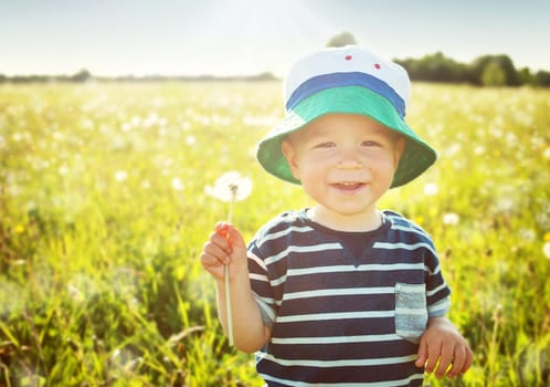 Baby boy sitting in grass on the fieald with dandelions at sunnysummer evening