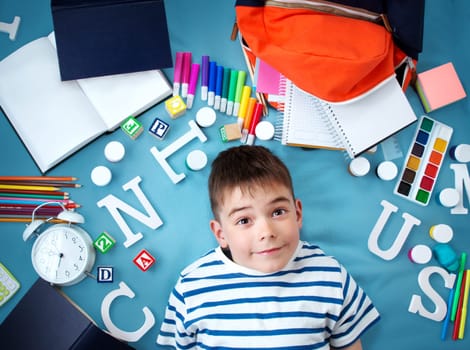 child lying on blue blanket with various school accessories