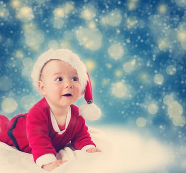 Eight month old baby in santa costume lying on soft blanket with blue background and falling snow