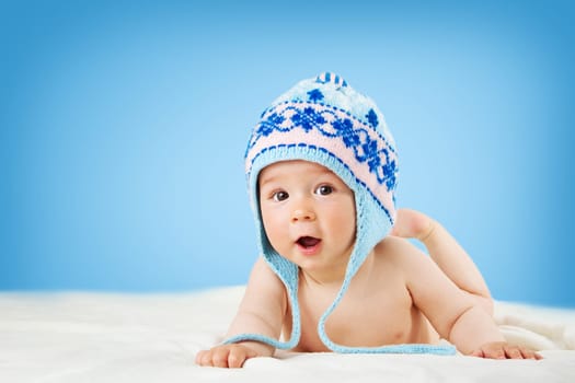 Eight month old baby in knitted winter hat lying on soft blanket with blue background