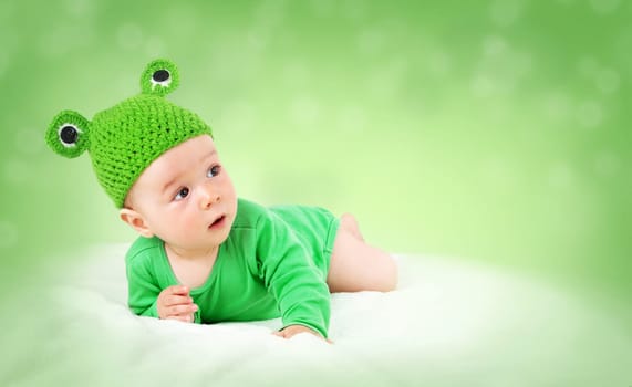 little baby in knitted frog hat on soft blanket on green background